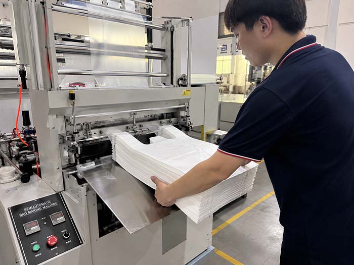 Operator manually removing finished bag stack from semi-automatic bag making machine after batch completion